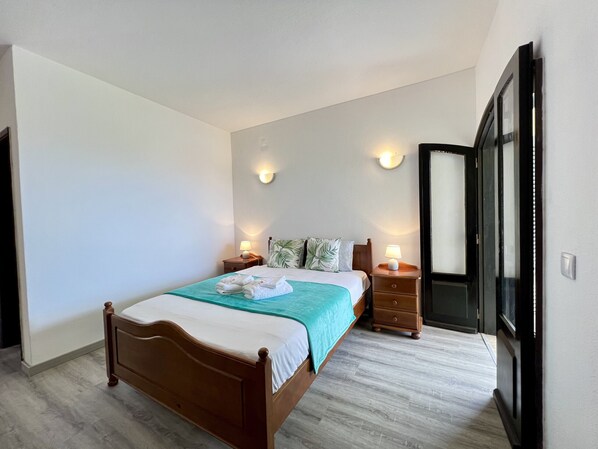 A neatly arranged bedroom with a wooden bed, two bedside tables with lamps, and a large mirror on the wall. - Carvoeiro Ocean Breeze by Homing (Lagoa)