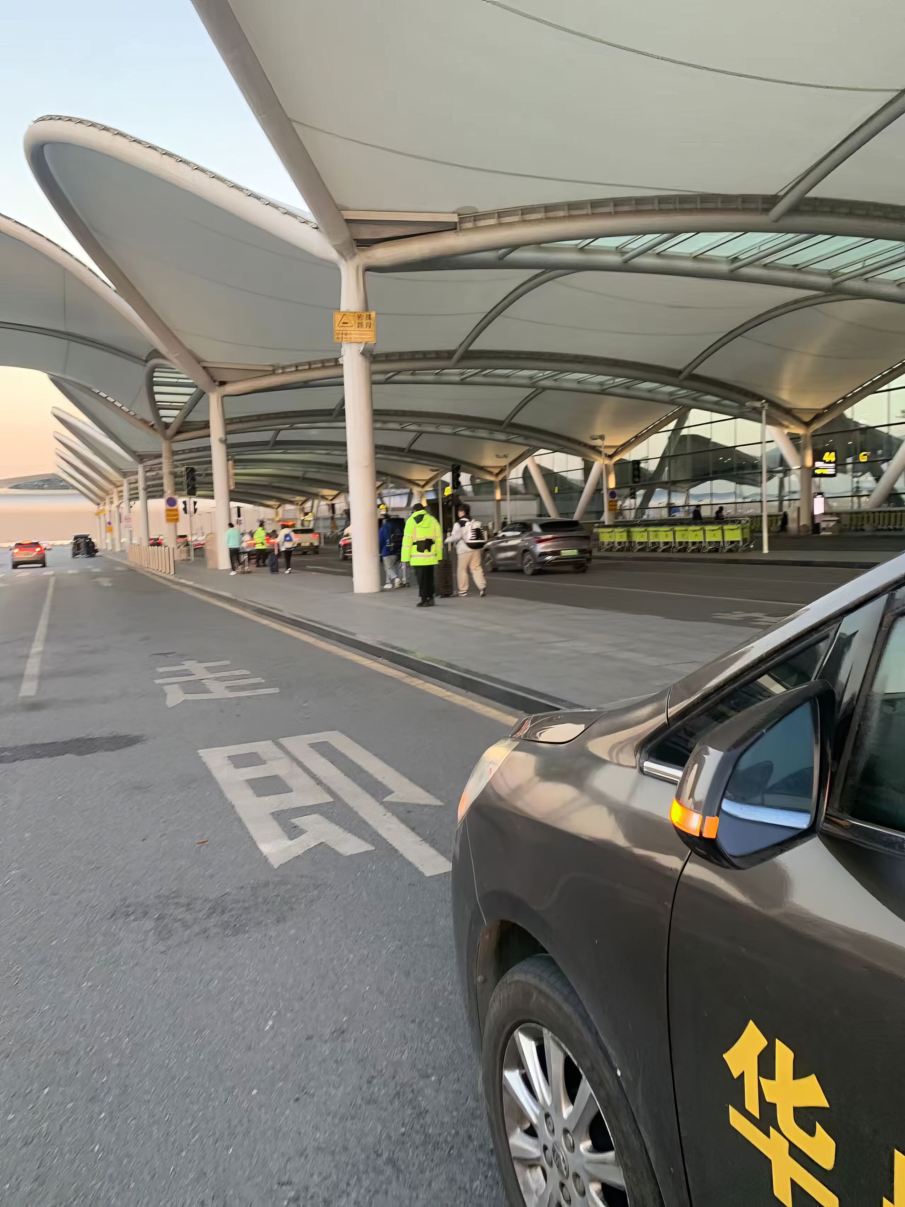 A modern airport terminal with a curved roof structure, a designated parking area, and a clear view of the sky.