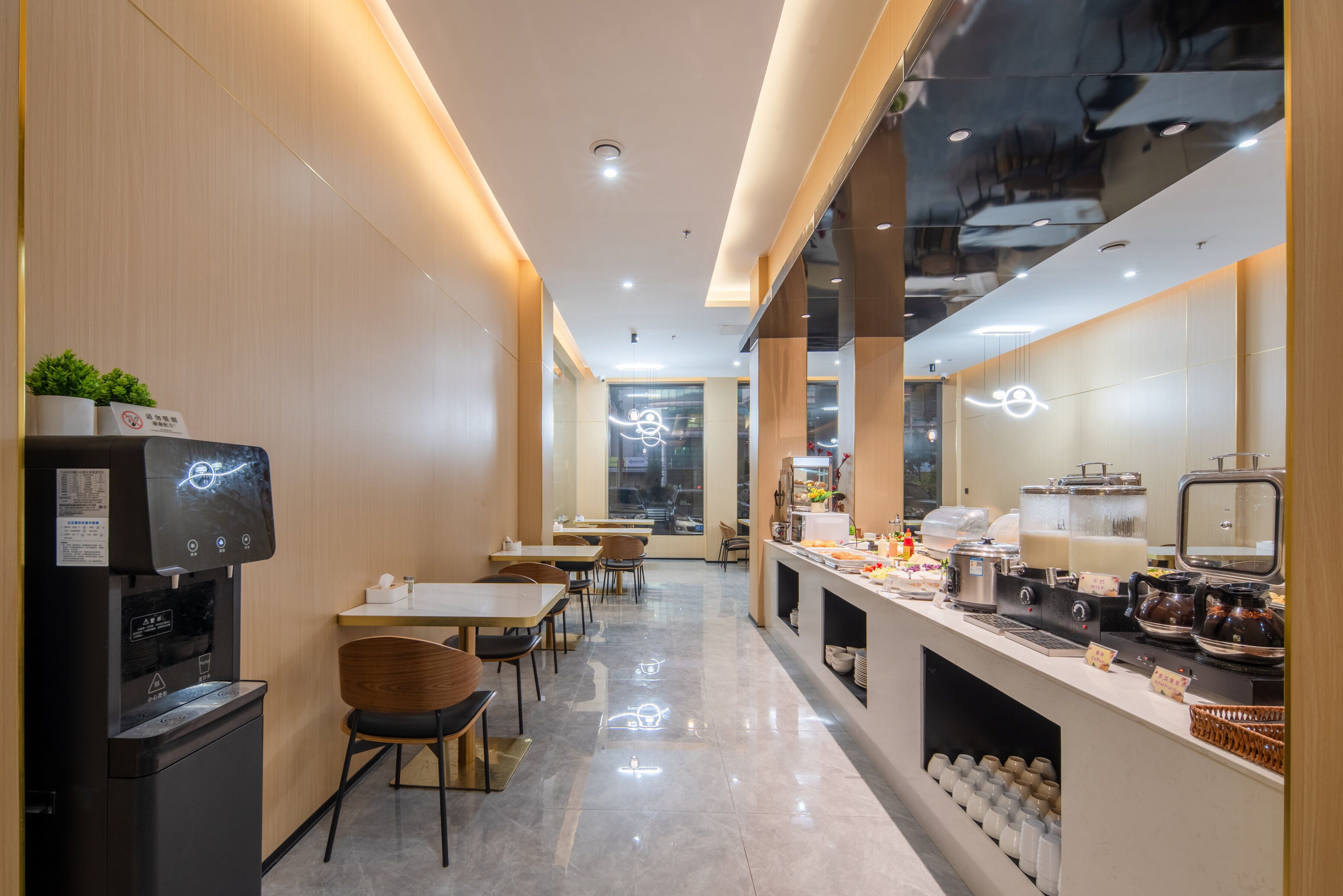 A modern cafe with a self-service coffee machine, seating area, and a counter with various food items.