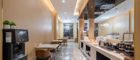 A modern cafe with a self-service coffee machine, seating area, and a counter with various food items.
