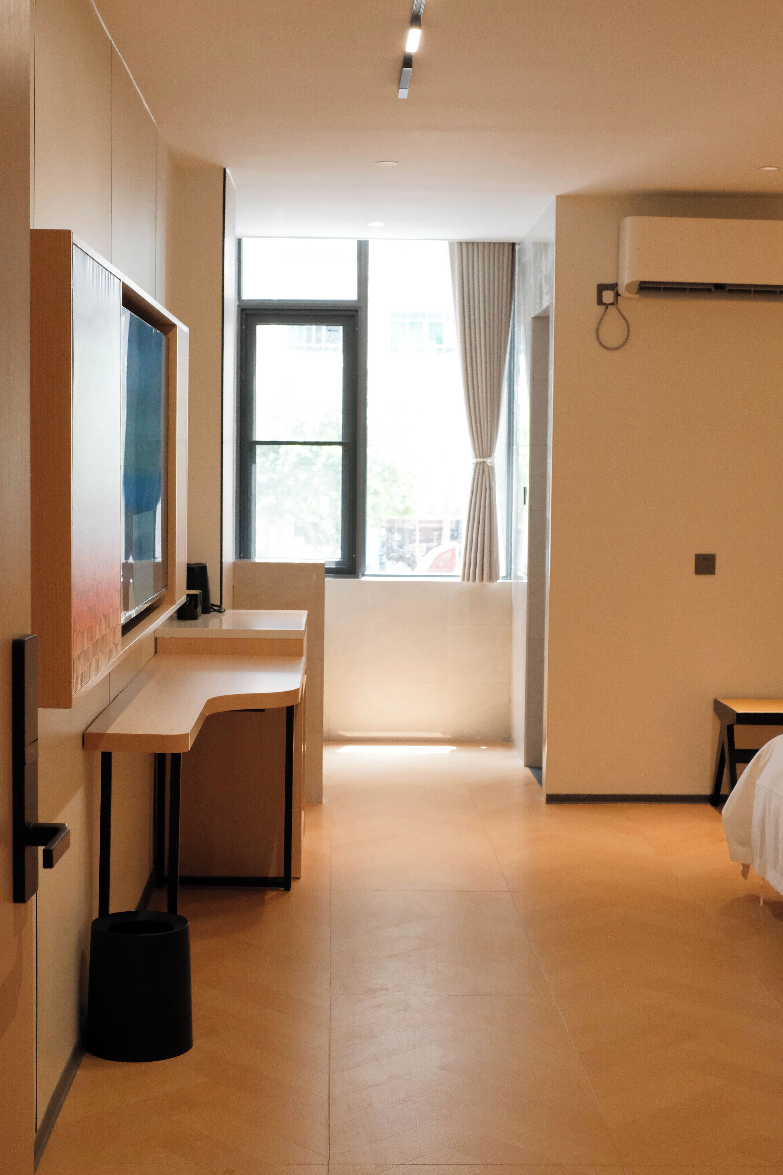 A hotel room with a desk, a bed, a TV, and a window with curtains.