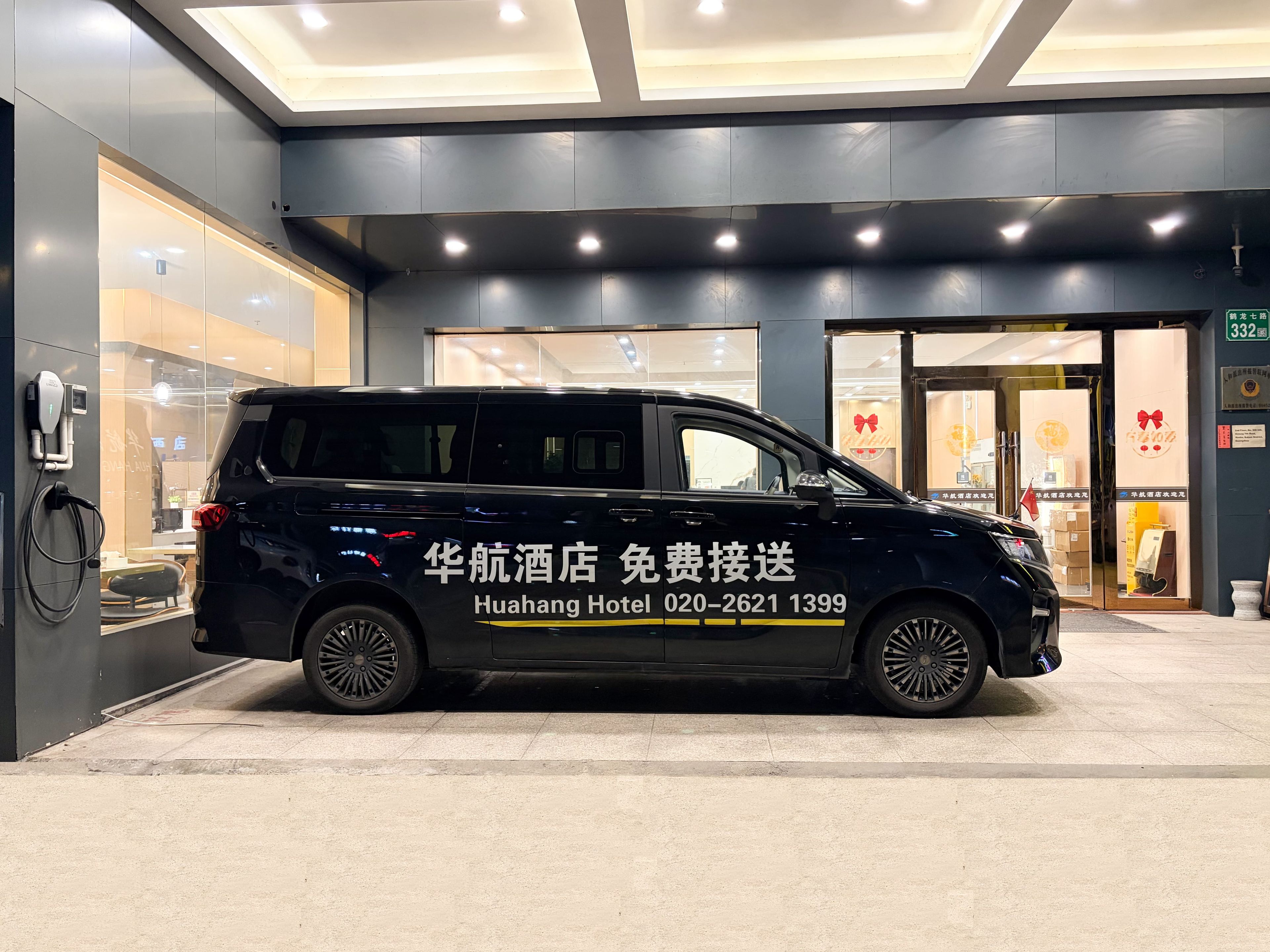 Un fourgon noir était garé devant l’entrée d’un hôtel, avec un numéro de téléphone et un panneau indiquant un service de navette gratuit.
