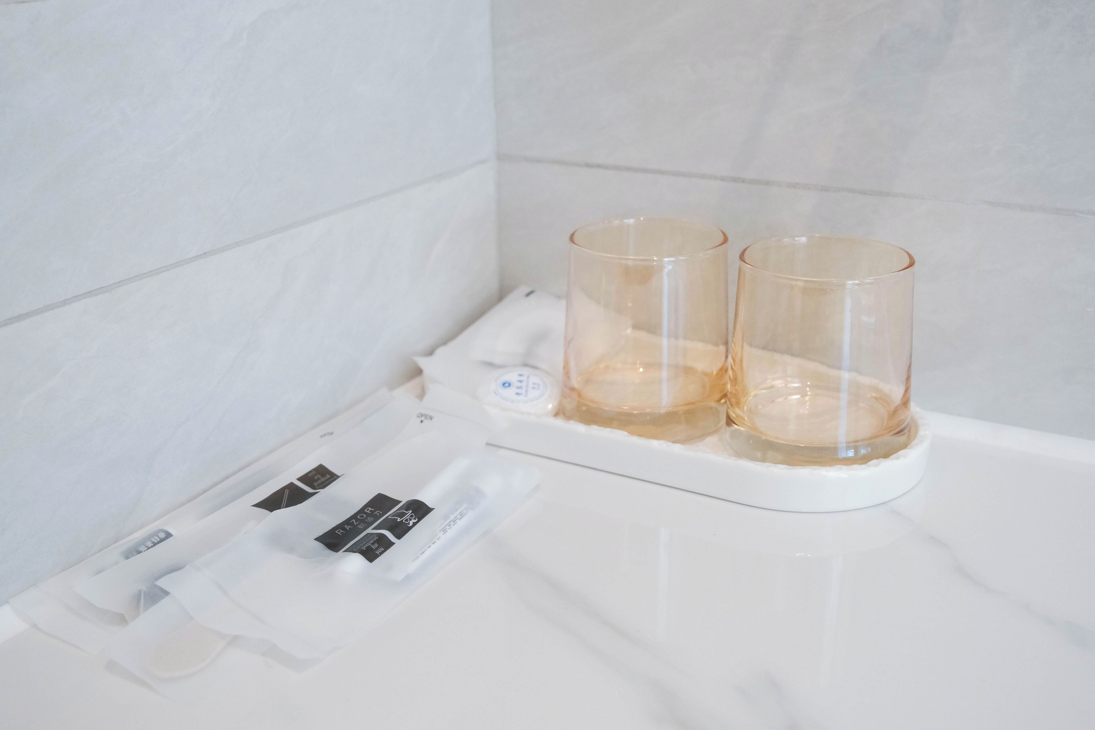 Casa de banho com bancada branca, dois copos de vidro transparente e um dispensador de sabonete.