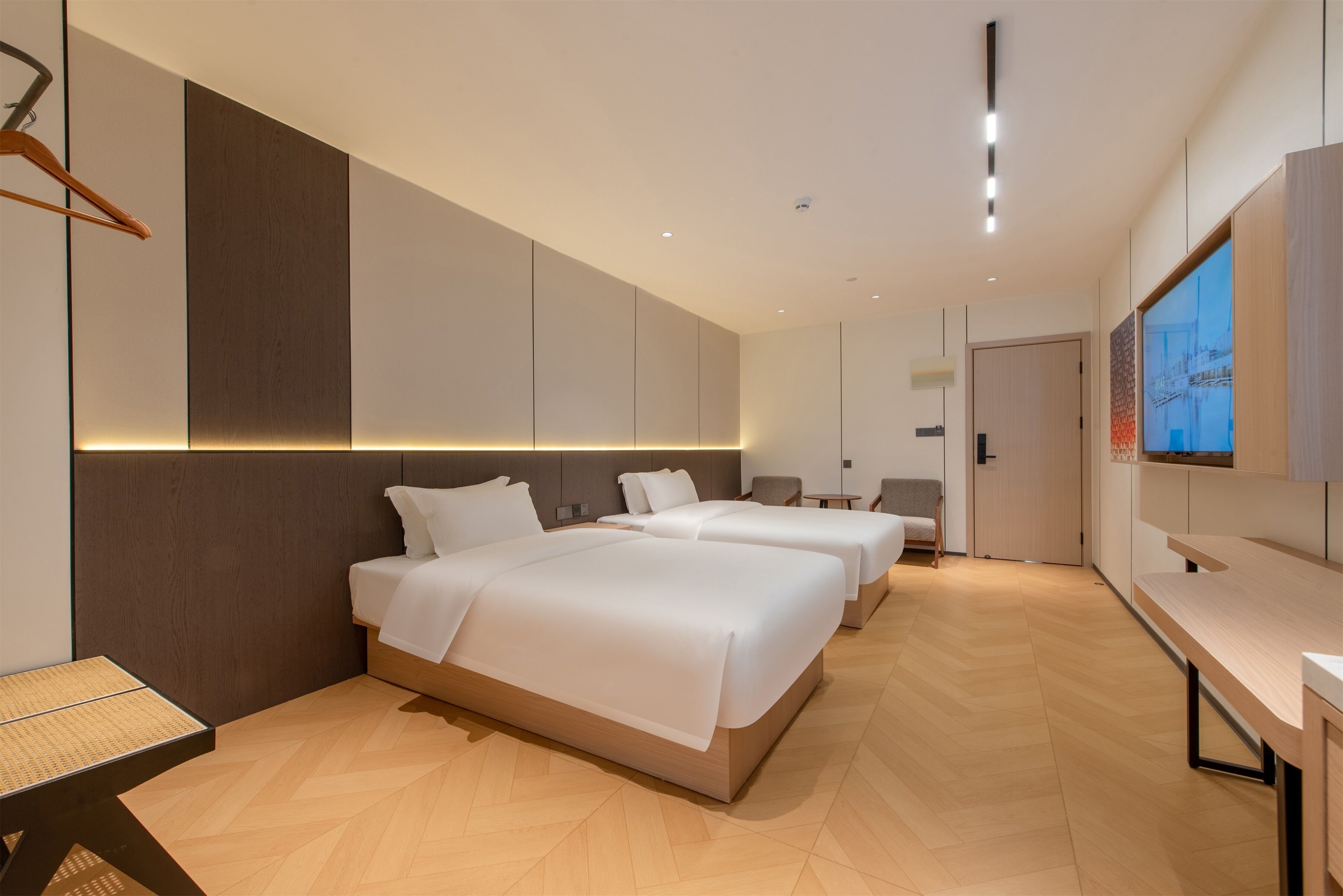 Una habitación de hotel moderna con dos camas, un escritorio y una amplia pantalla de televisión.