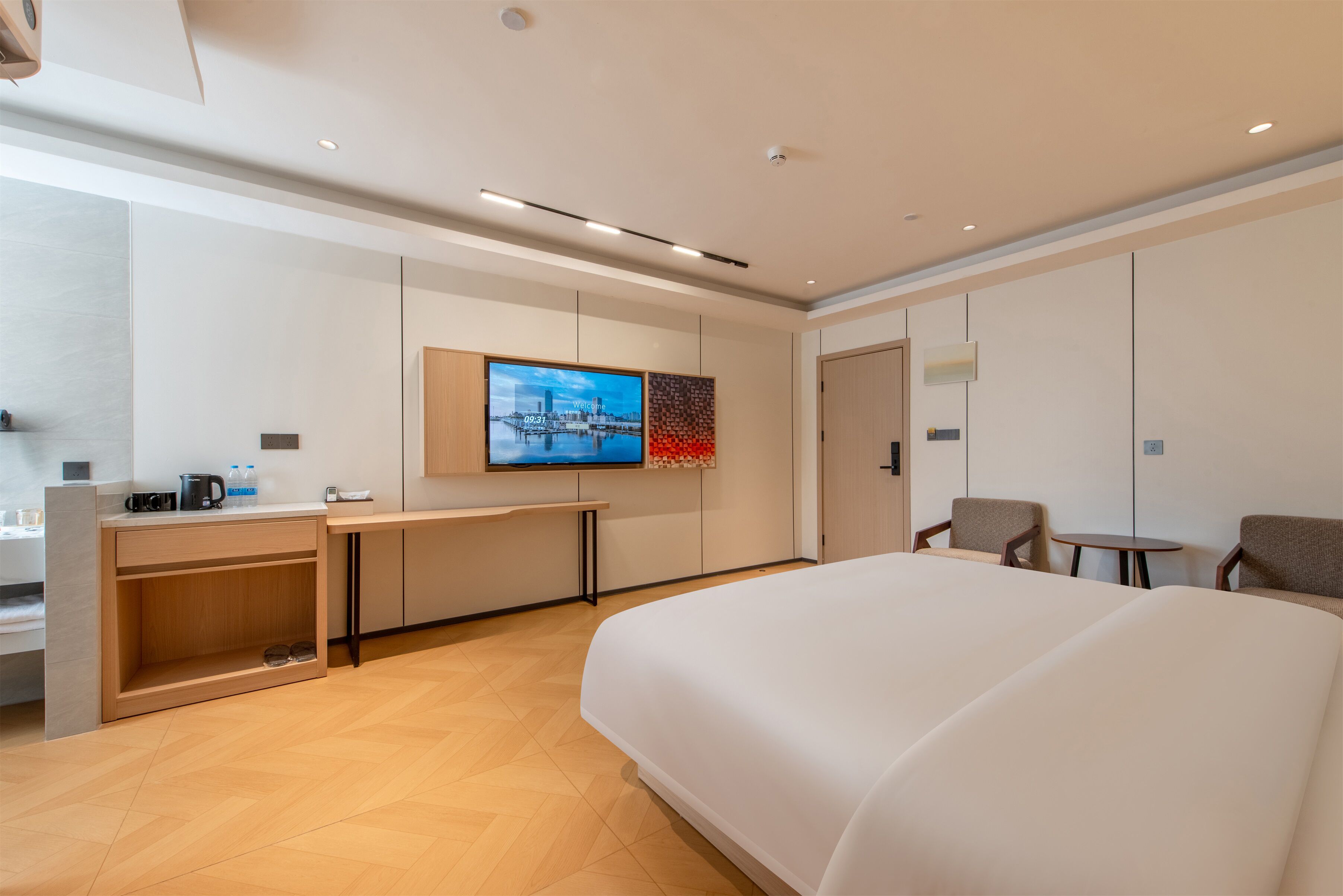 A modern hotel room with a large bed, a desk with a flat-screen TV, a small table, and two chairs.