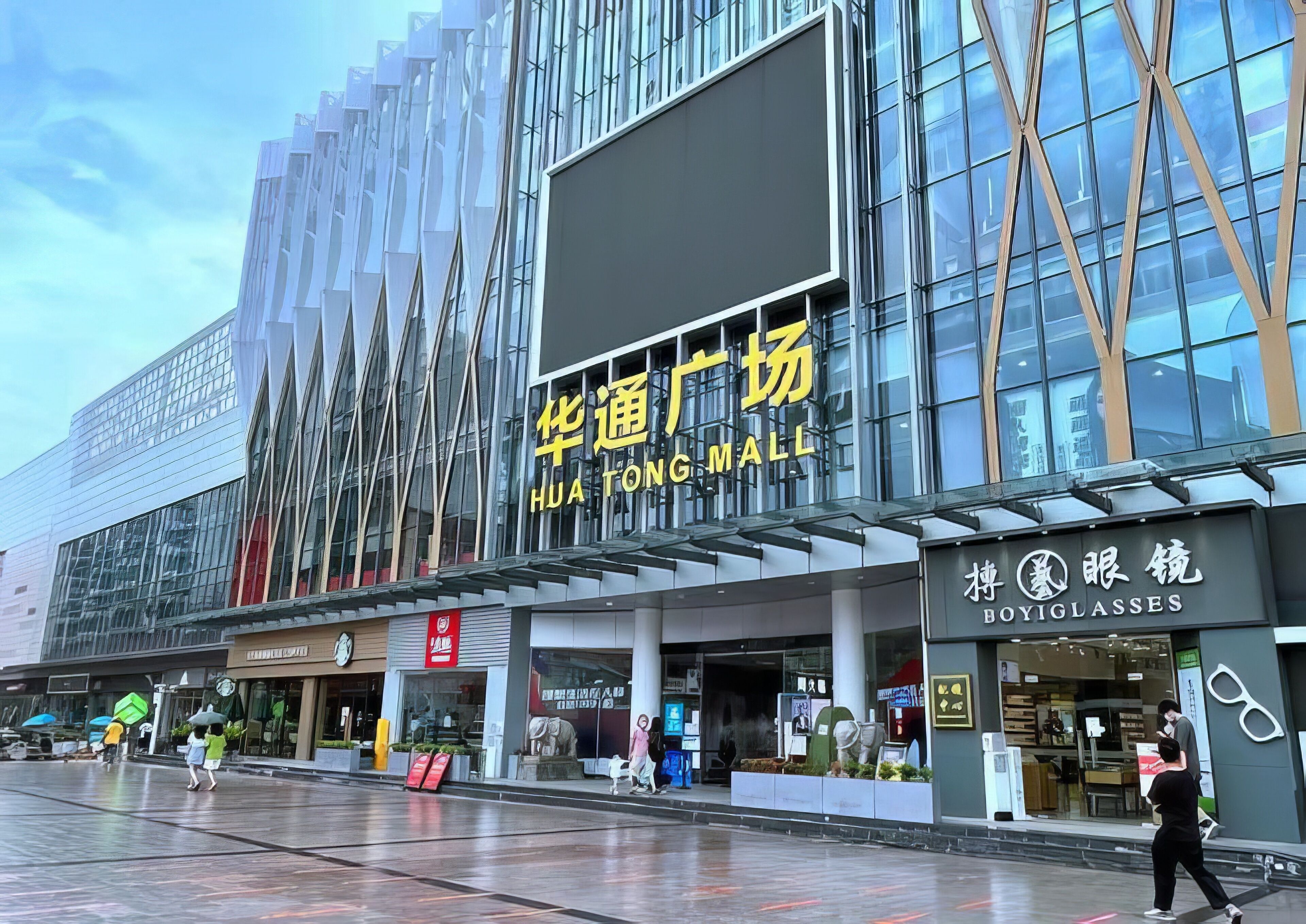 A modern building with a large glass facade and signage for Hua Tong Mall and Boyiglasses.