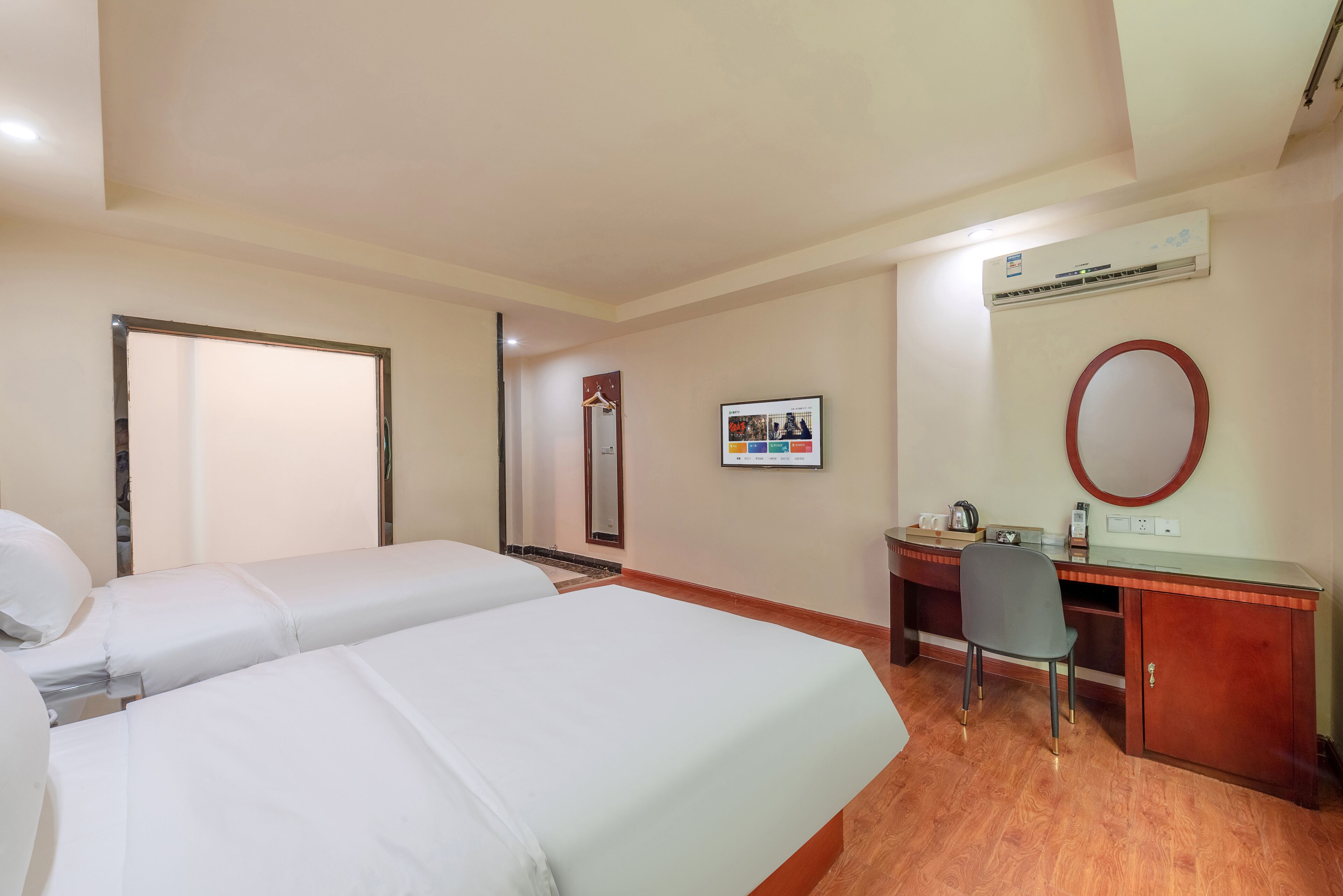Une chambre d’hôtel avec deux lits, un bureau, une chaise, un miroir, un appareil de climatisation et une photo encadrée accrochée au mur.