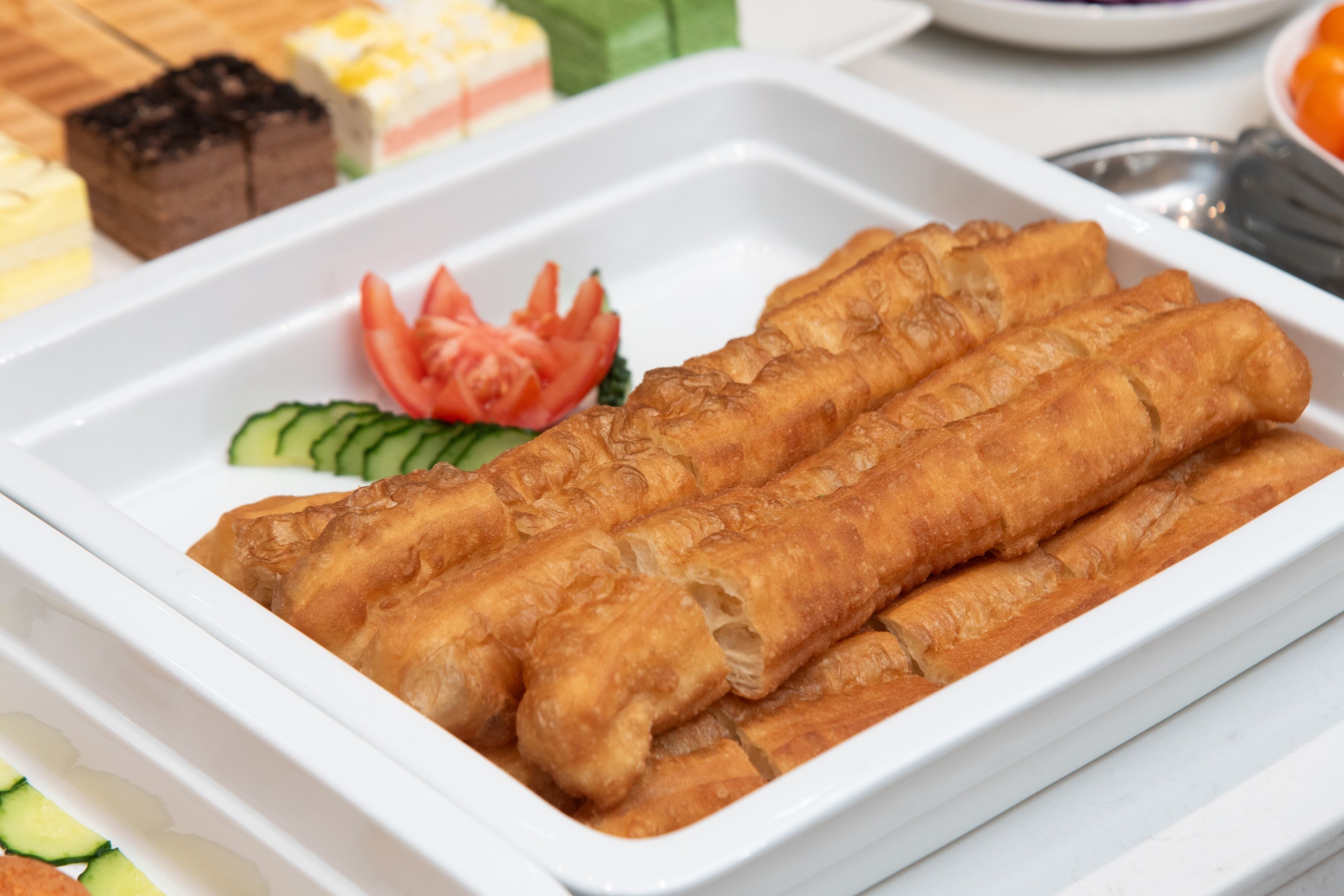 Una bandeja de rollitos de primavera fritos, acompañados de pepino y tomate en rodajas.
