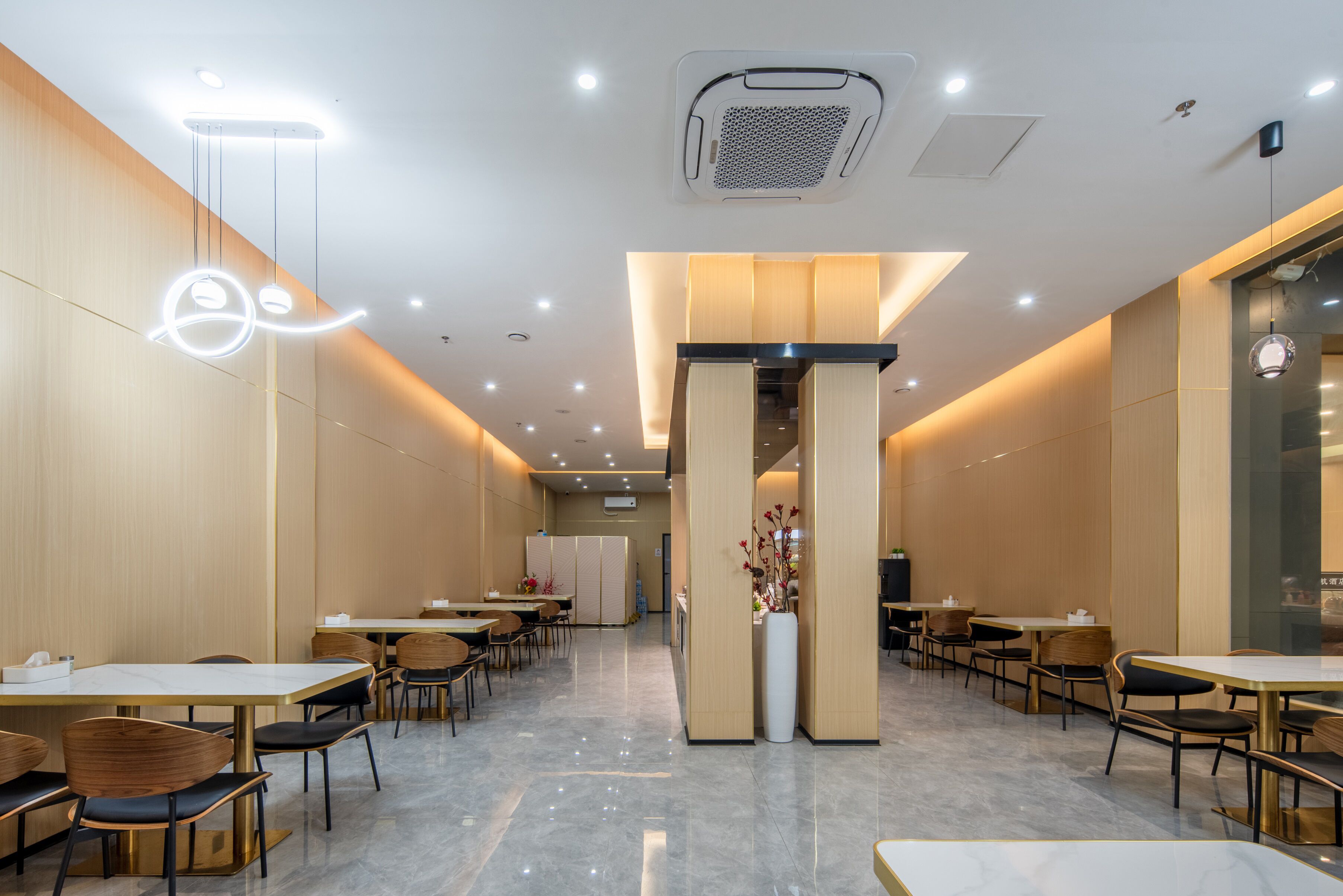 A modern dining area with tables and chairs, a central column with a vase, and recessed ceiling lighting.