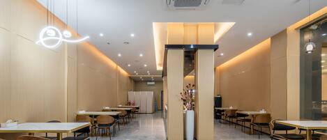 A modern dining area with tables and chairs, a central column with a vase, and recessed ceiling lighting.