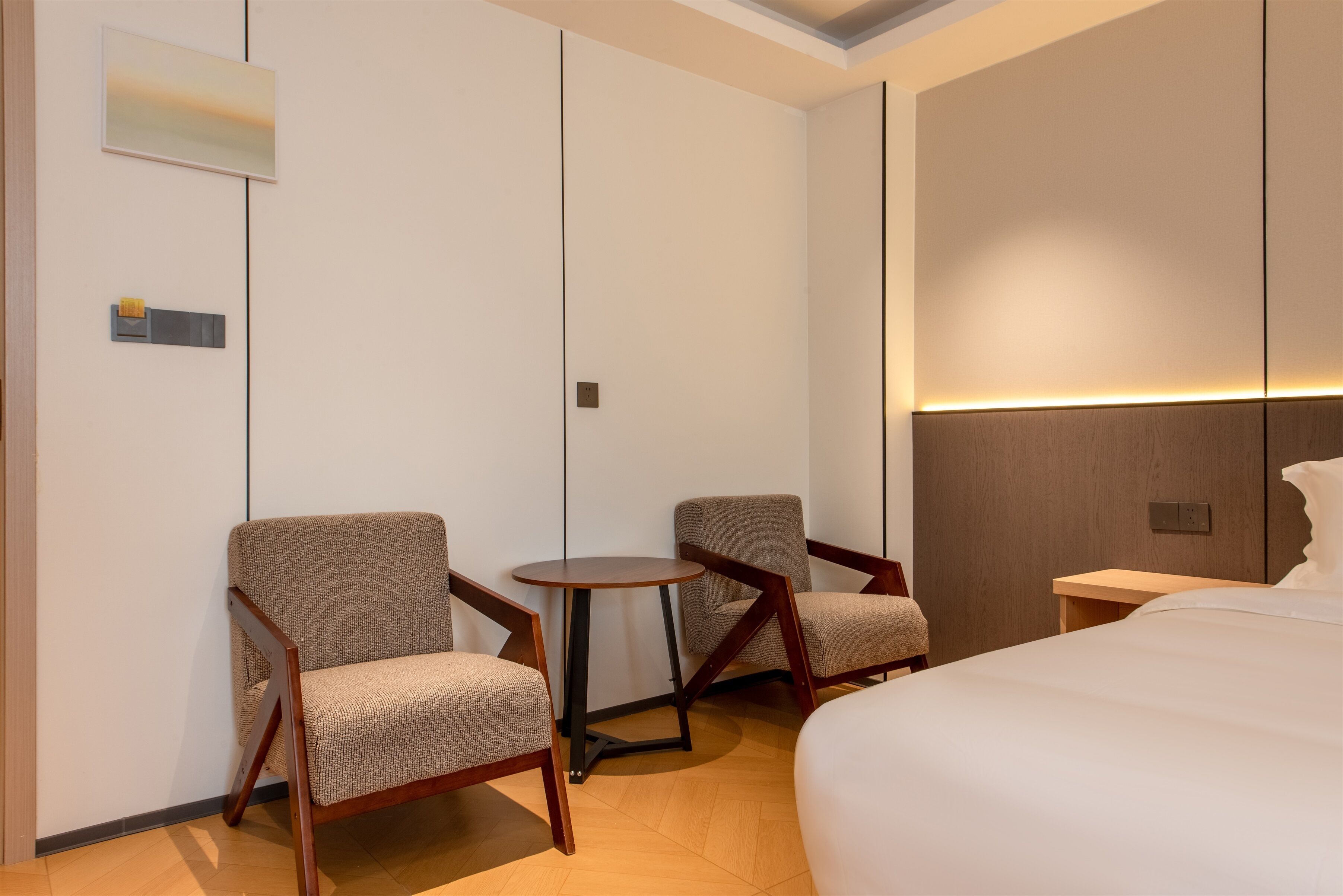 A hotel room with a large bed, two armchairs, a small round table, and a wall-mounted TV.