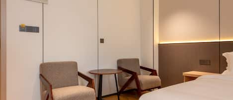 A hotel room with a large bed, two armchairs, a small round table, and a wall-mounted TV.