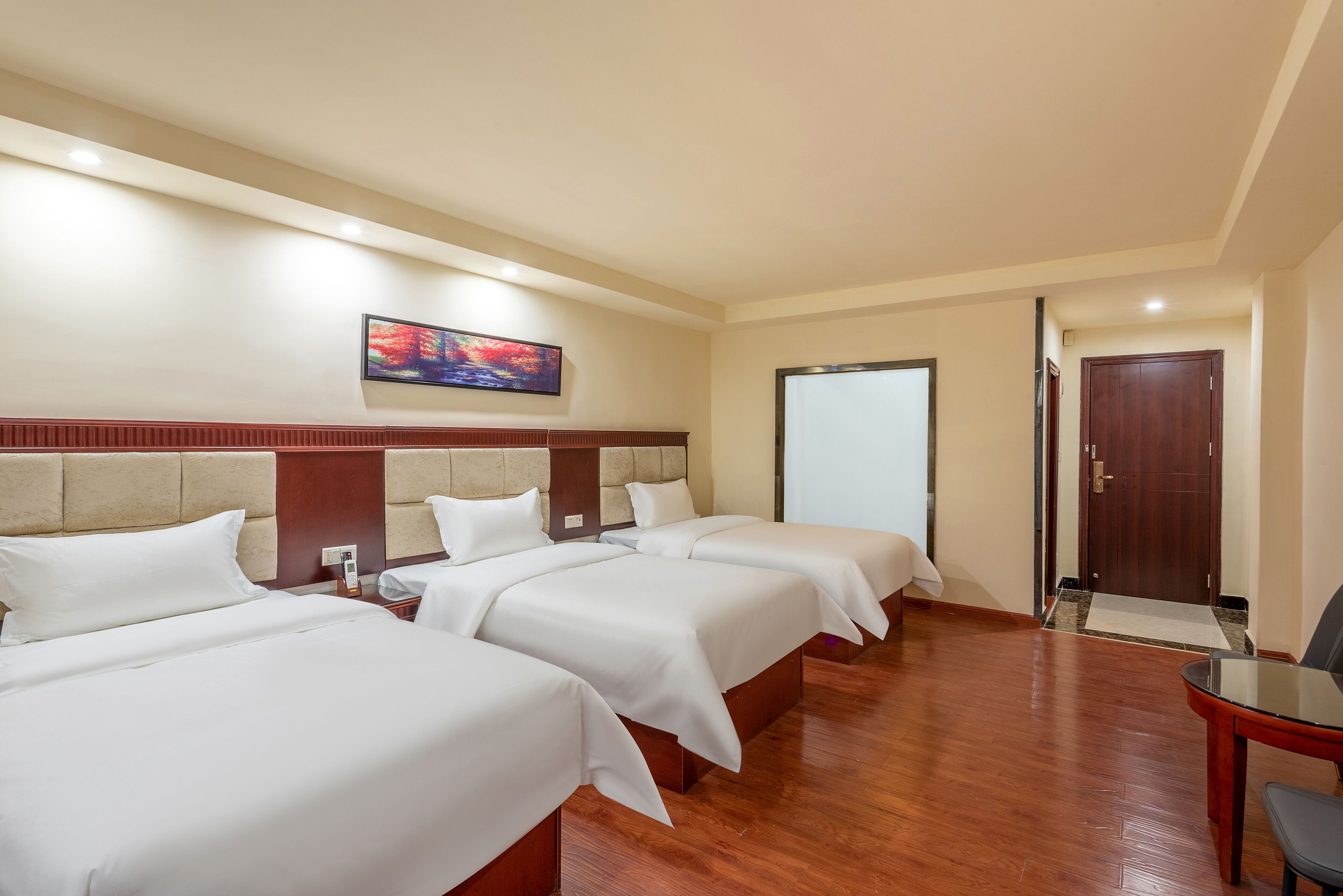 A hotel room with three beds, a flat-screen TV, a wooden door, and a small table.