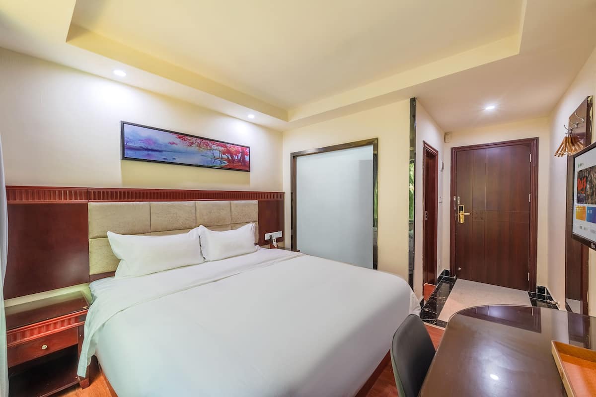 Een hotelkamer met een groot bed, een bureau, een stoel, een nachtkastje, een garderobe en een schilderij aan de muur.