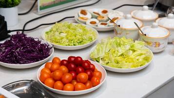 Ein Buffet mit verschiedenen Speisen, darunter Salate, Kirschtomaten und Schalen mit farbenfrohem Gemüse.