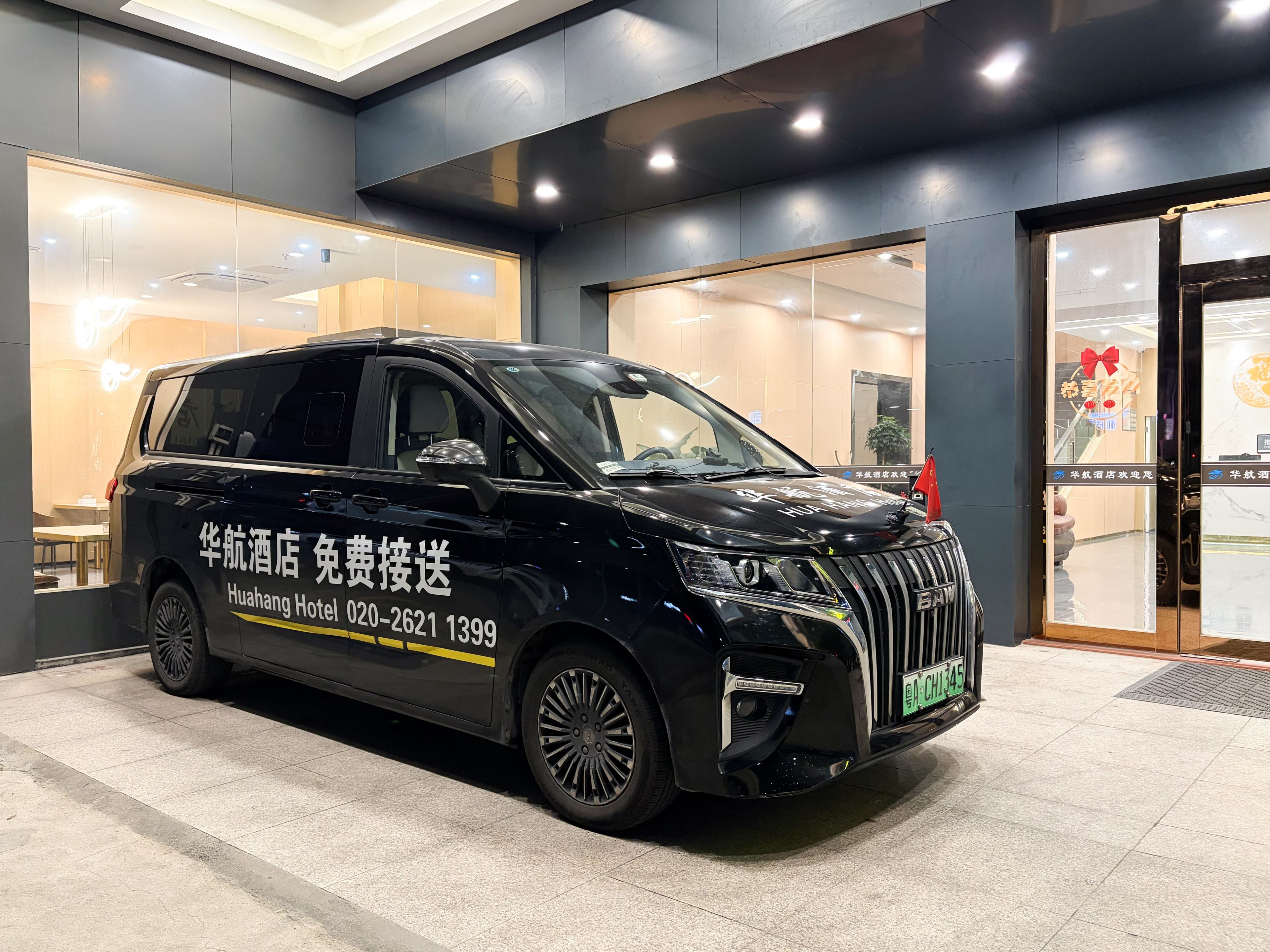 A black van with 'Huanghe Hotel' branding parked in front of a hotel entrance.