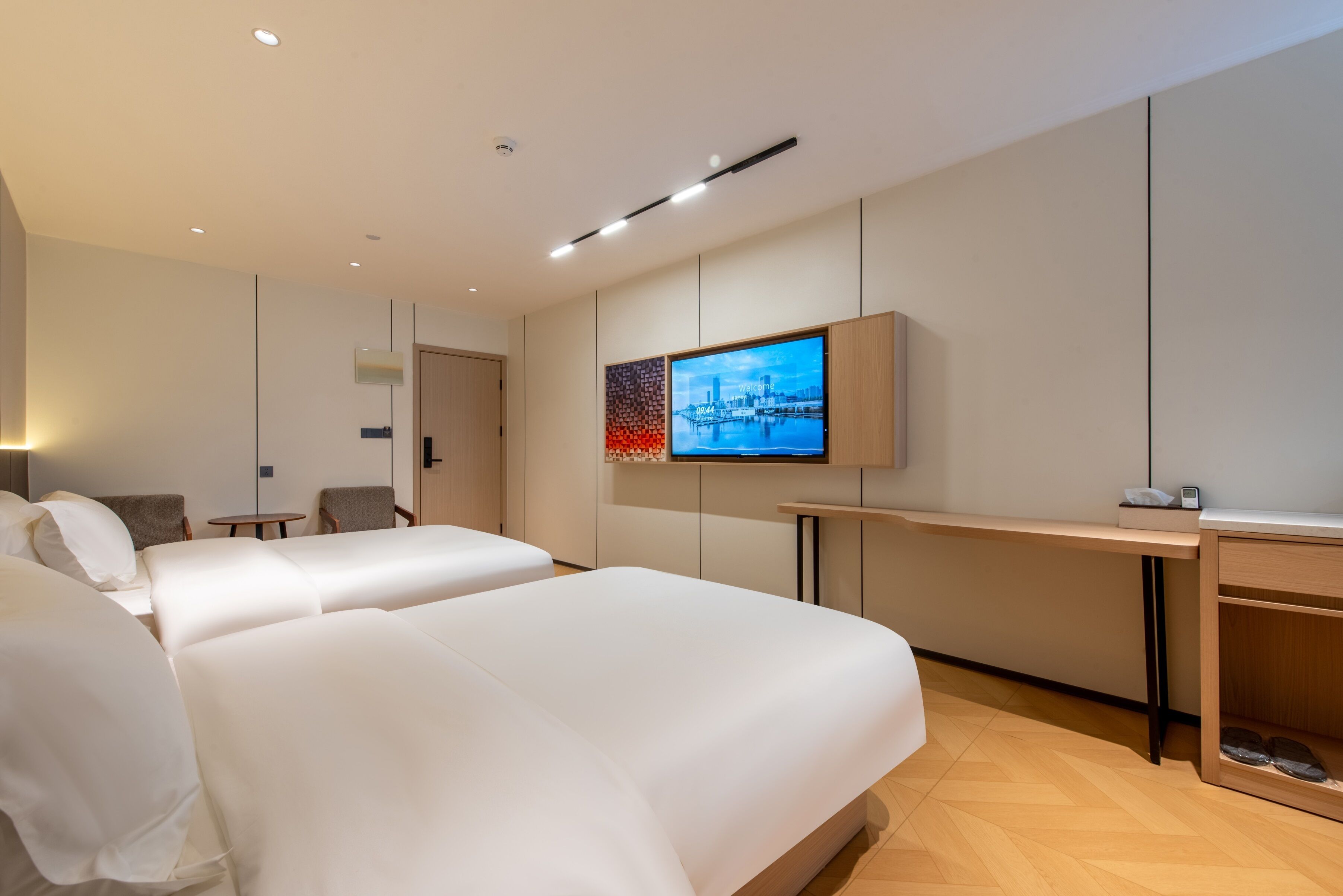A modern hotel room with two large beds, a desk, a television, and a small table.
