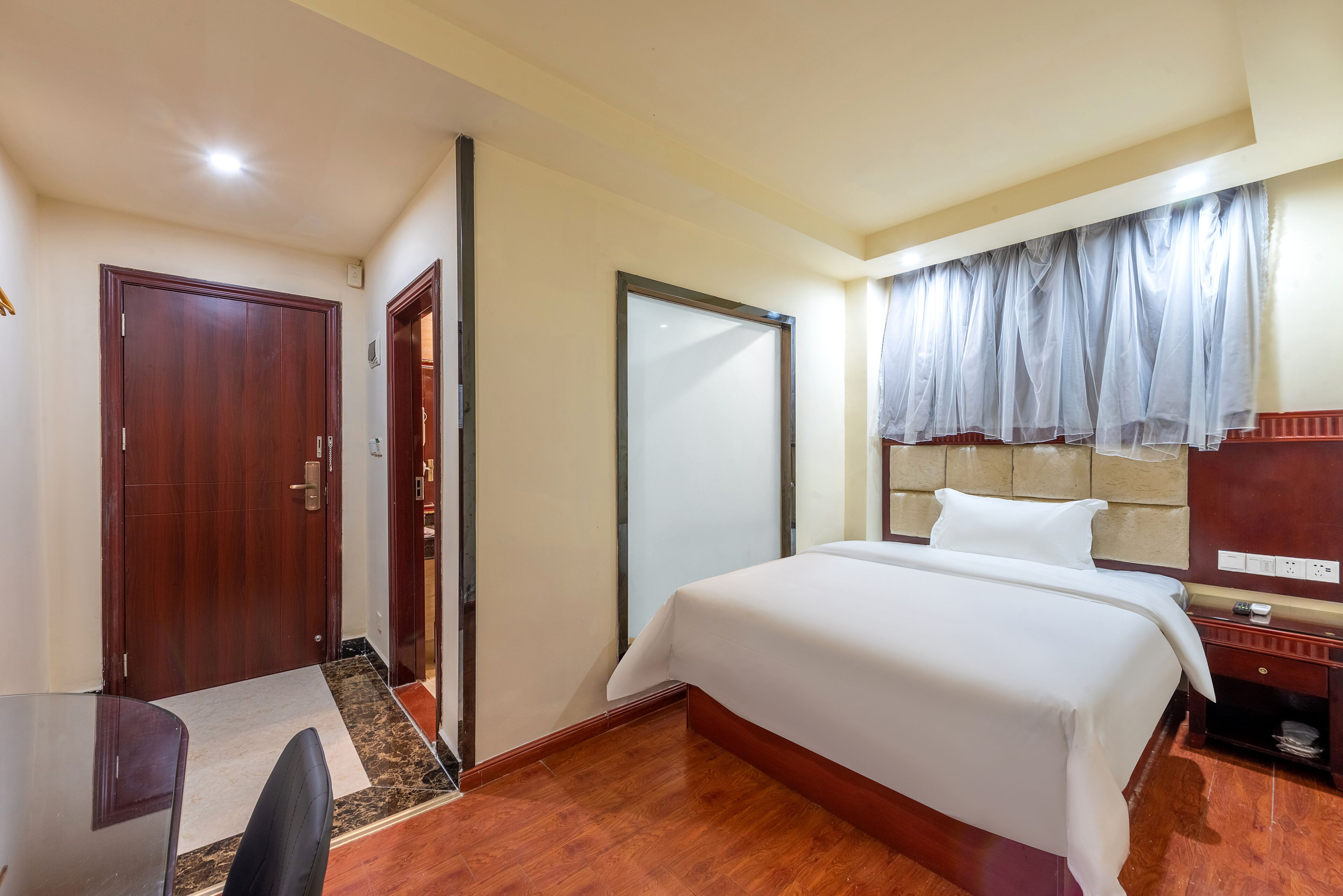 Habitación de hotel con una cama grande, un escritorio y una silla. Cuenta con un armario, un espejo y una ventana con cortinas.