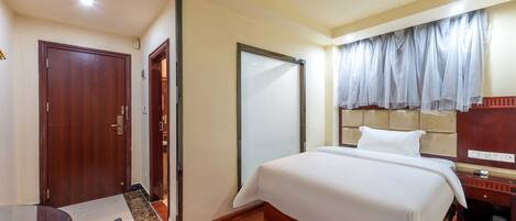 Habitación de hotel con una cama grande, un escritorio y una silla. Cuenta con un armario, un espejo y una ventana con cortinas.