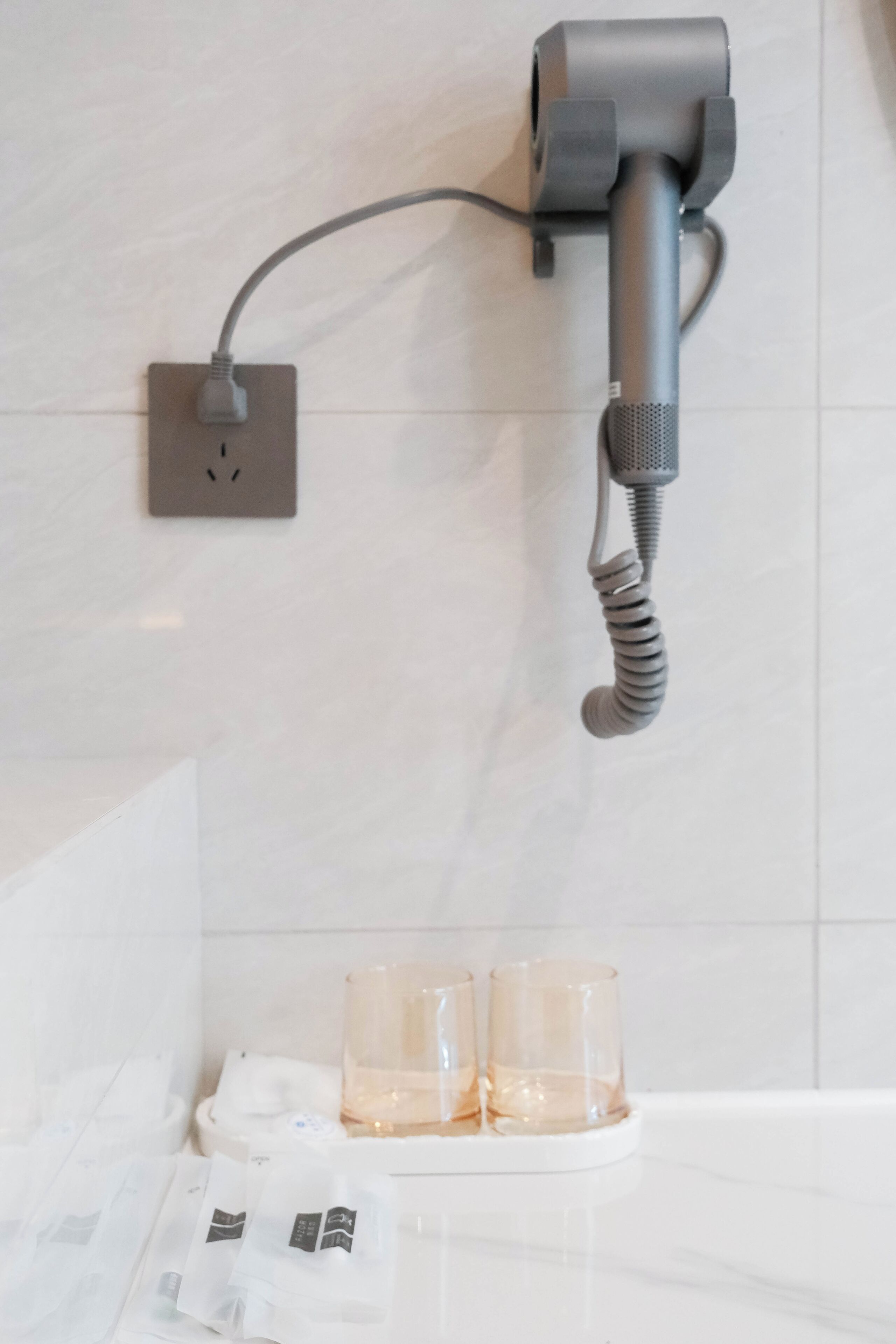 Ein Badezimmer mit einem an der Wand befestigten Fön, einem Handtuchhalter und zwei Gläsern auf einem Tablett.