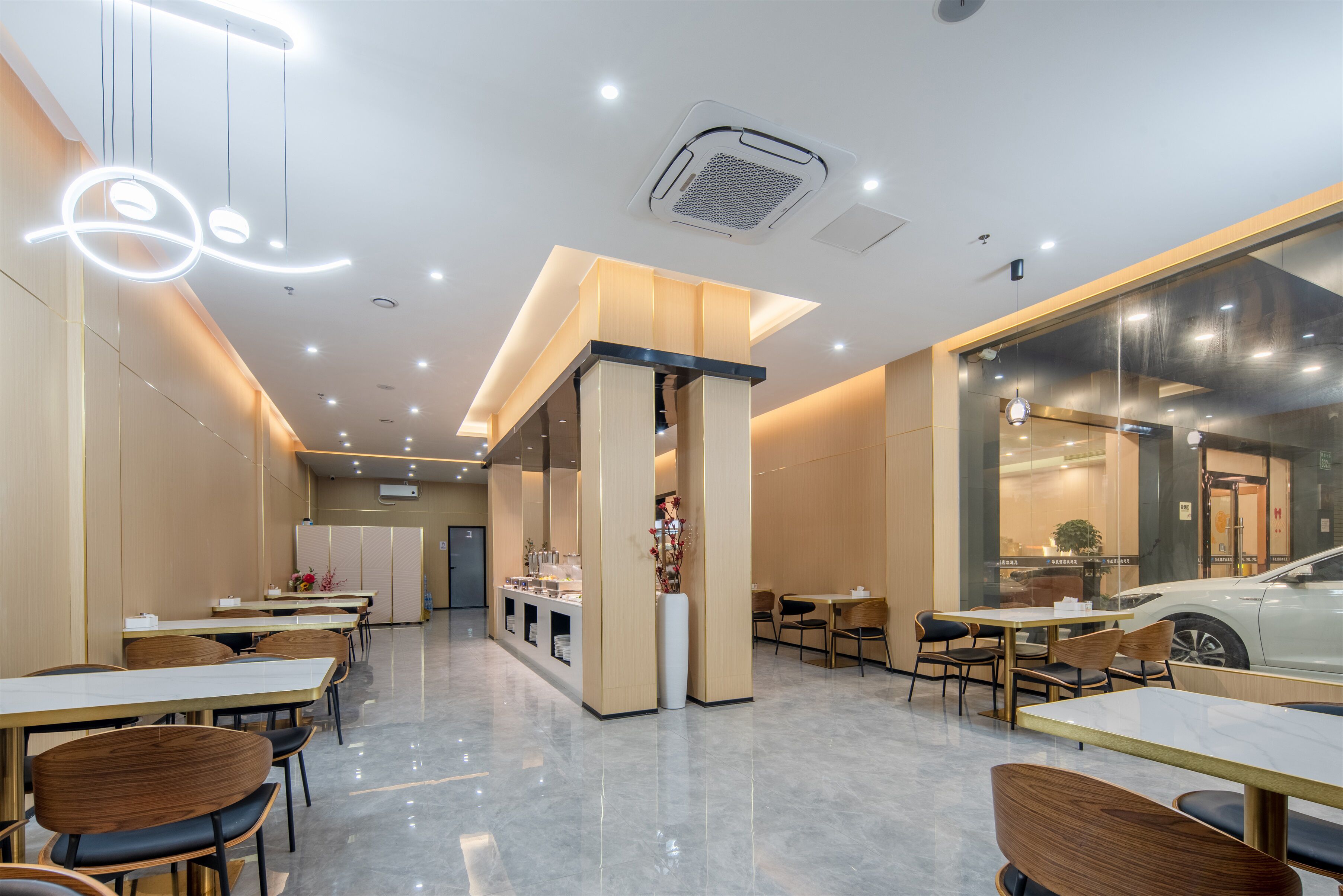 A modern restaurant interior with marble flooring, wooden tables and chairs, and a central counter with a decorative vase.
