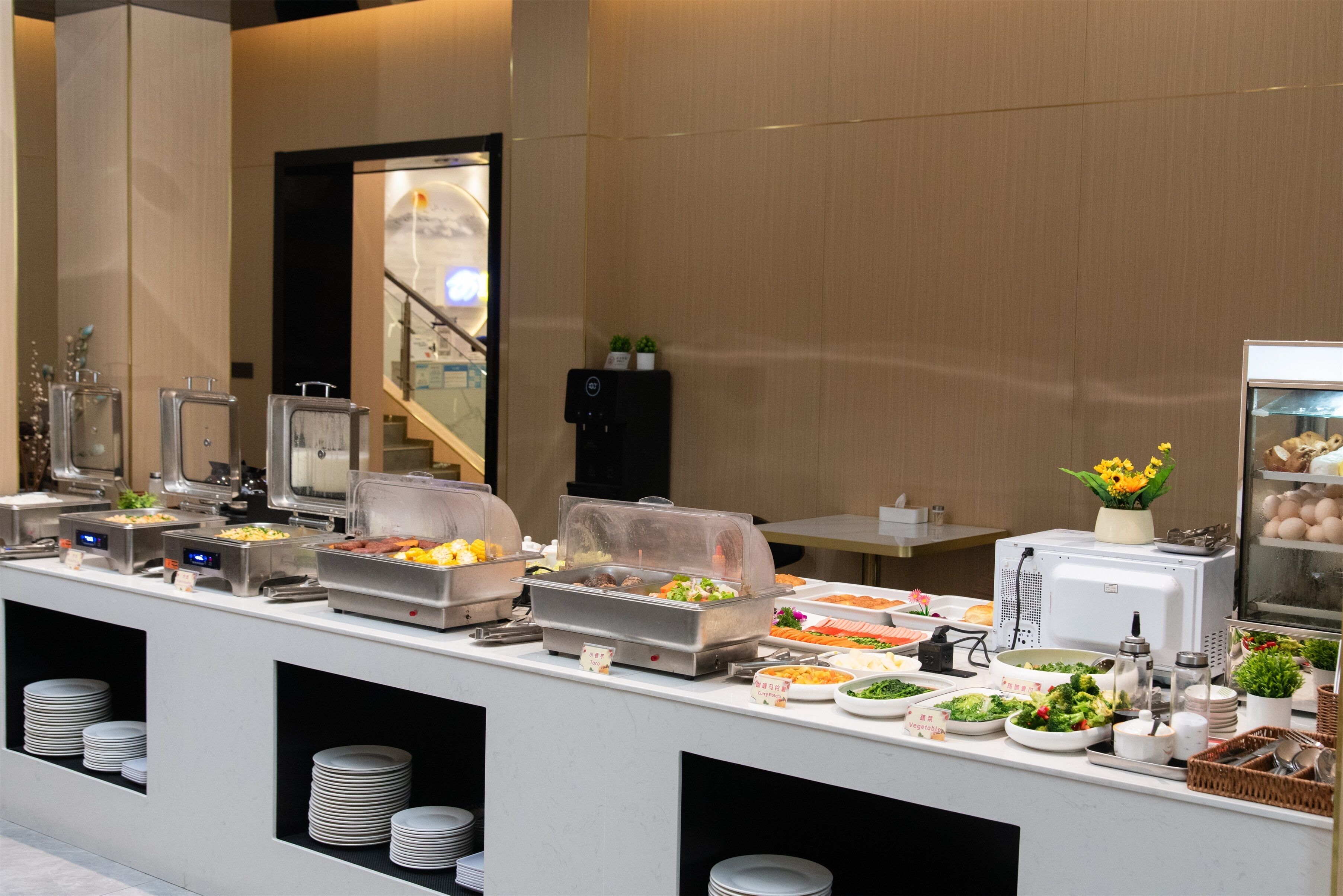 Un'impostazione a buffet con diverse postazioni gastronomiche, tra cui insalate, frutta e piatti caldi, disposti su un bancone con piatti e utensili per servire.