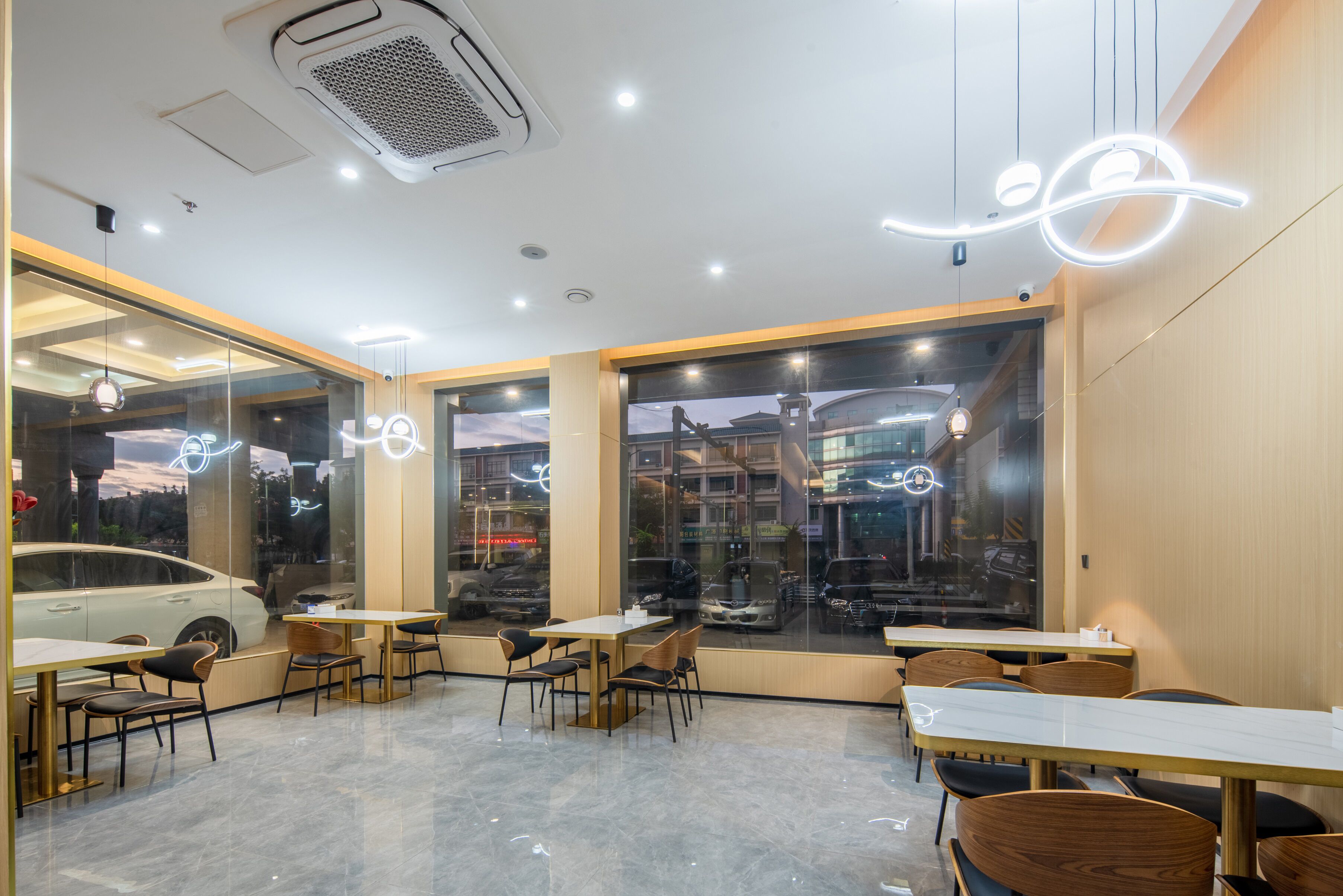 A modern restaurant interior with tables and chairs, large windows with city views, and decorative lighting.