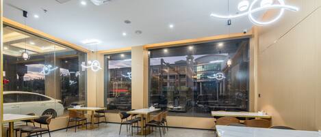 A modern restaurant interior with tables and chairs, large windows with city views, and decorative lighting.