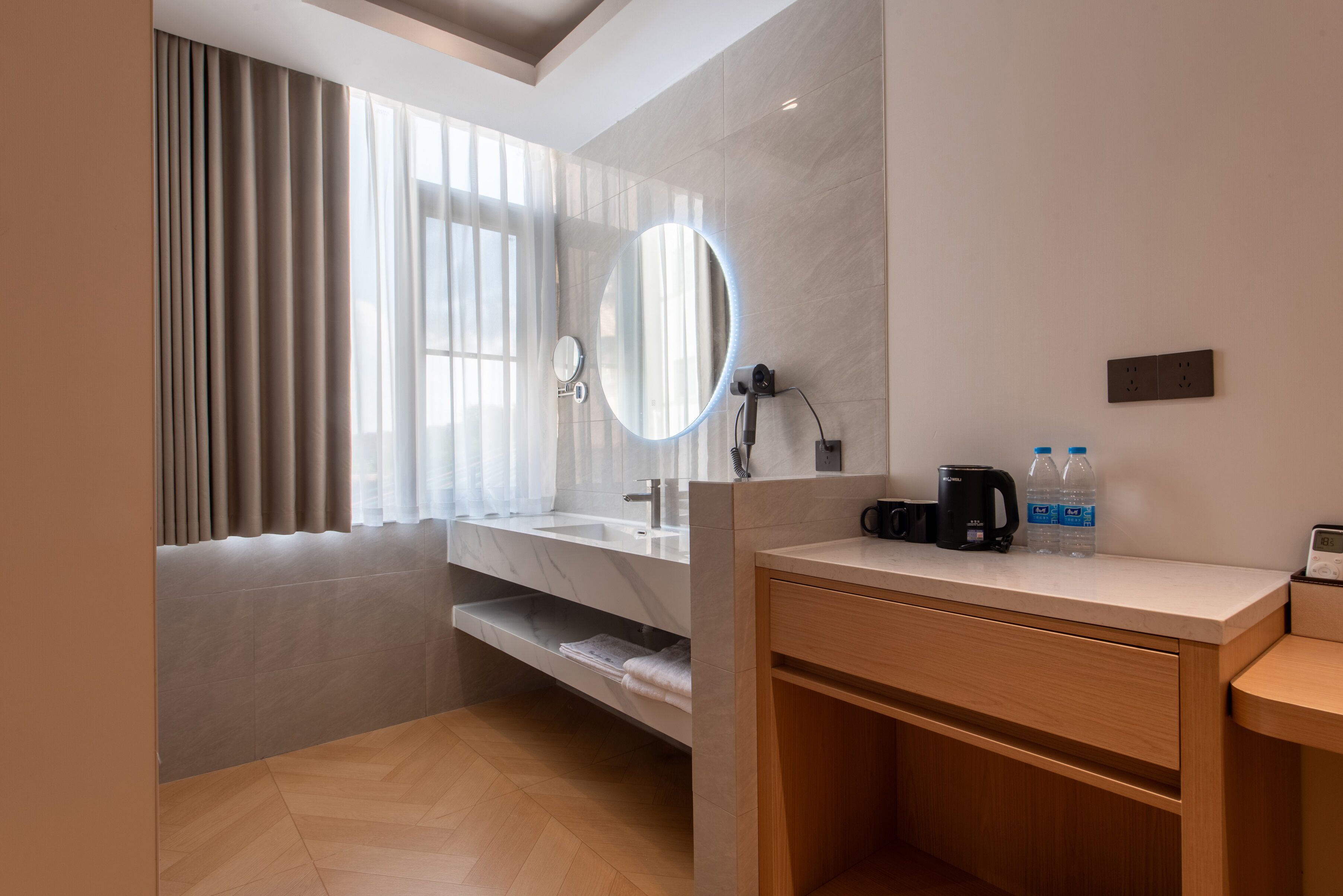 A modern bathroom with a vanity, sink, and mirror. There are two bottles of water and a coffee maker on the counter.