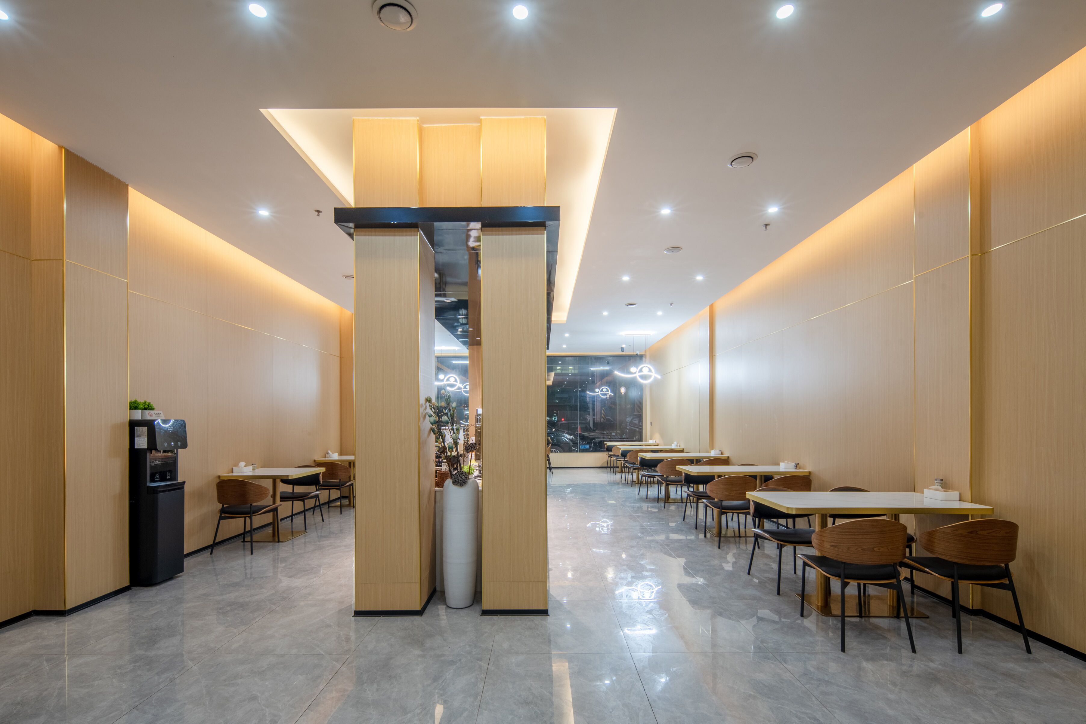 Un restaurant modern amb una columna central, taules, cadires i una màquina expenedora.