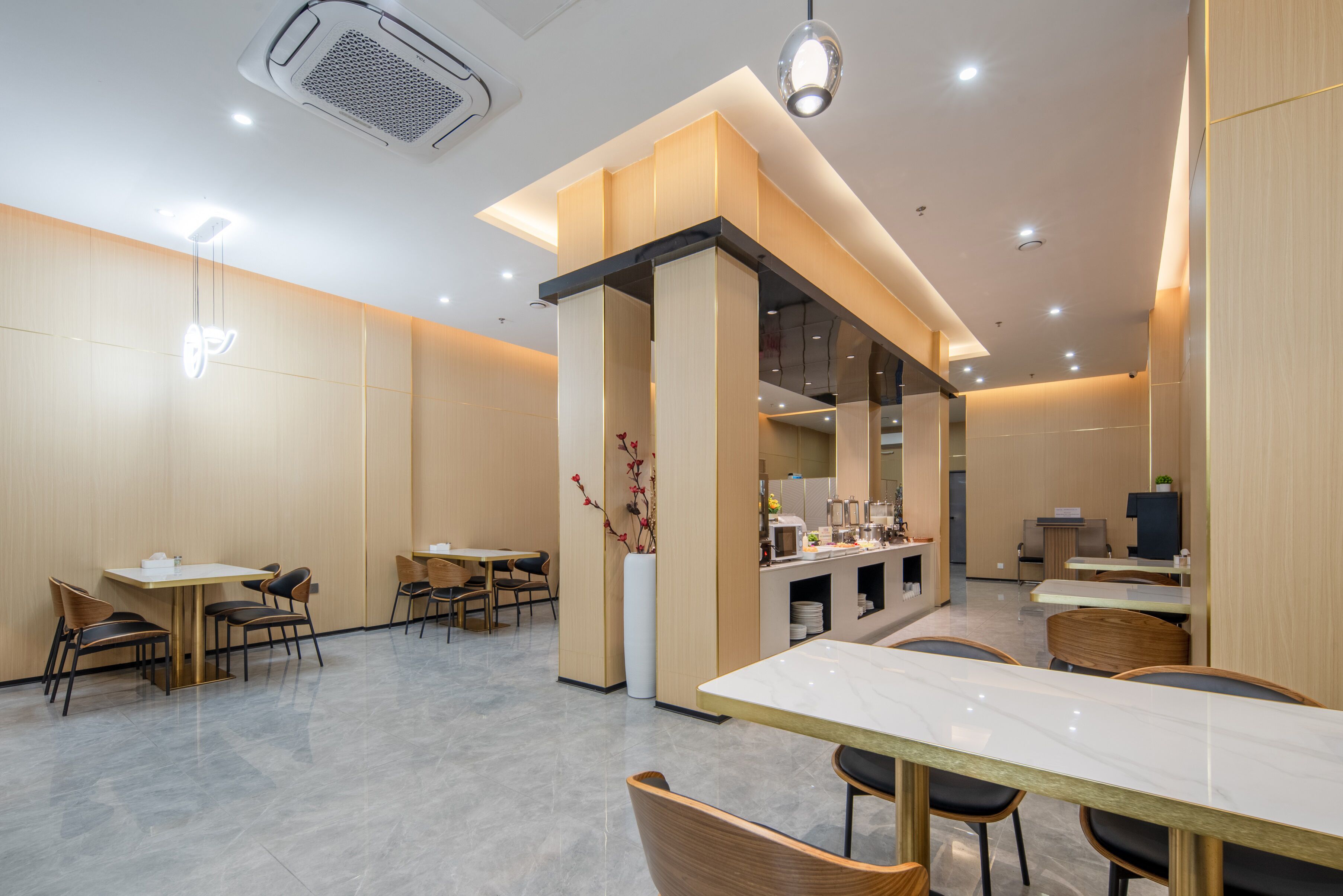A modern restaurant with multiple dining tables and chairs, a central counter, and a decorative vase.