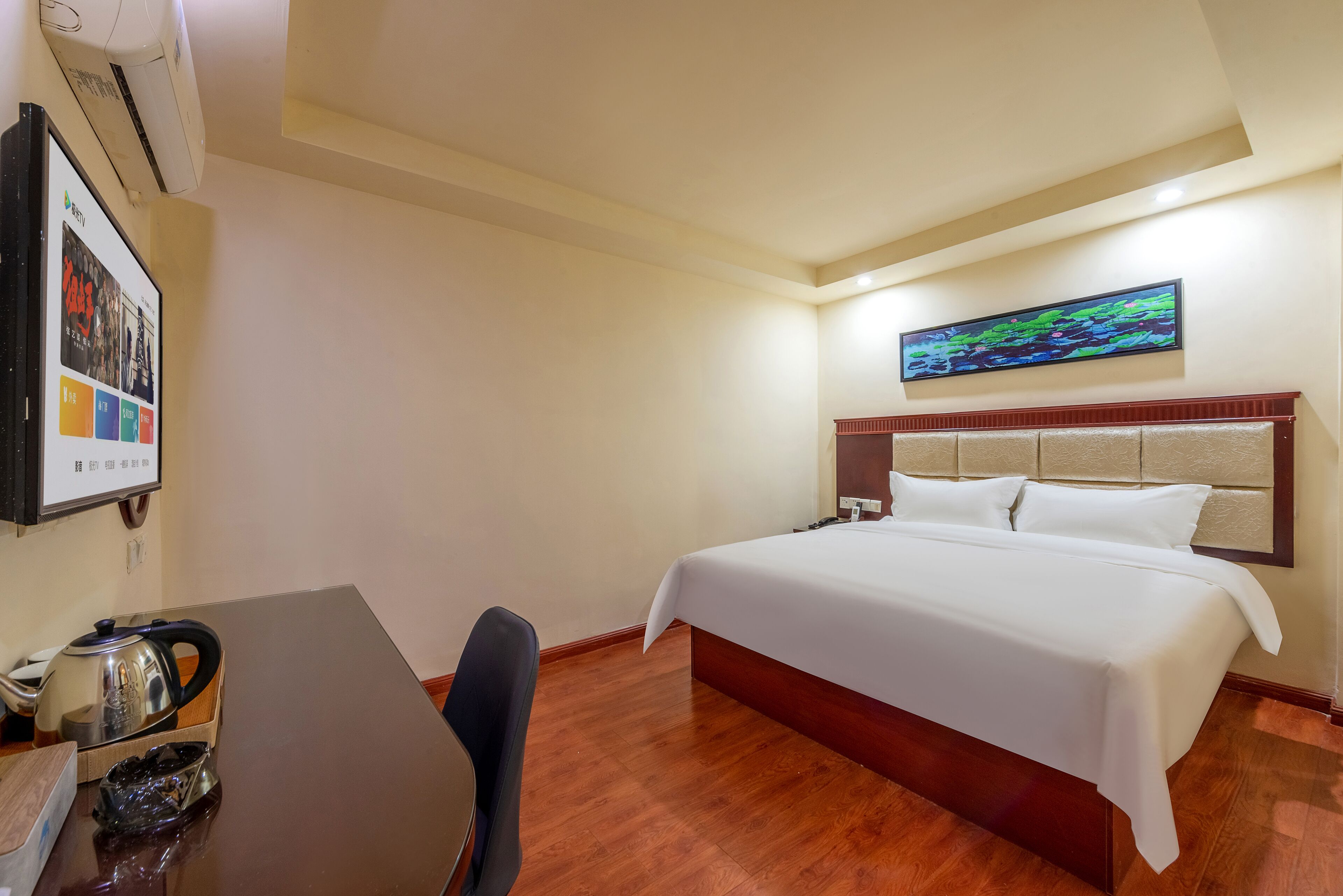 Ein Hotelzimmer mit einem Bett, einem Schreibtisch mit Wasserkocher, einem Sessel und einem an der Wand montierten Fernseher.