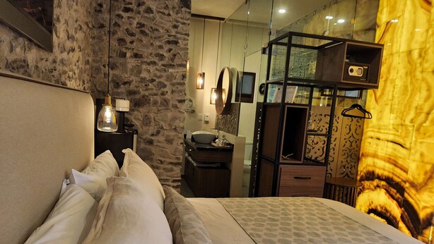 A bedroom with a stone wall, a bed with white linens, a wooden dresser, and a mirror. - Castello di Carlo - Suite Carlo IV (Val'Quirico)
