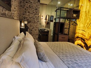 A bedroom with a stone wall, a bed with white linens, a wooden dresser, and a mirror. - Castello di Carlo - Suite Carlo IV (Val'Quirico)