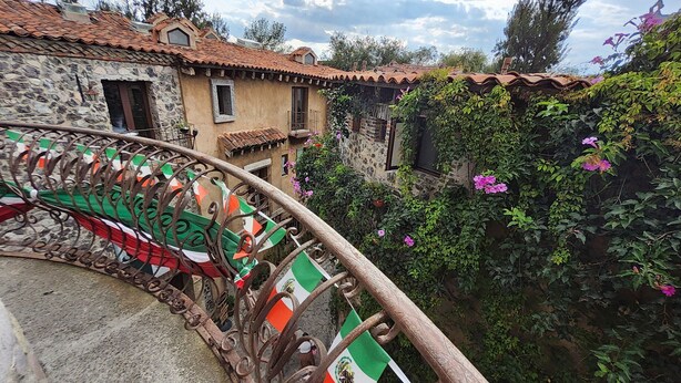 A stone building with a tiled roof, a wrought iron railing with flags, and a garden with flowering plants. - Castello di Carlo - Suite Carlo IV (Val'Quirico)