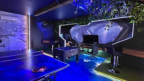 A room with a foosball table, a large screen, and a wall with a mural. - Fabulous Disney Vacation Home - 8bd - Private Pool w SPA - Near to Disney (Kissimmee)