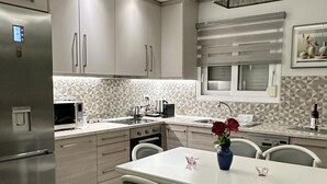 A modern kitchen with a central island, stainless steel appliances, and a dining area with a white table and chairs. - Luxurious Apartment with a sea view balcony in the N.Rhodes Yachting Marina Area (Rhodes)