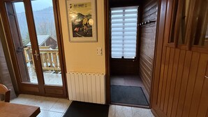 Un interior de madera con una puerta que da a un balcón, un cartel enmarcado en la pared y una ventana con persianas.
