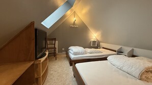 Un dormitorio con techo inclinado, televisor, escritorio y dos camas.