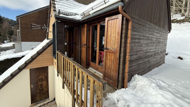 Una cabaña de madera con un porche, techo de metal y puerta de madera.