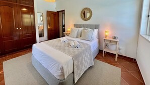 A bedroom with a large bed, a wooden wardrobe, a mirror, and a bedside table with a lamp. - Vilamoura White House Villa by Homing (Loulé)