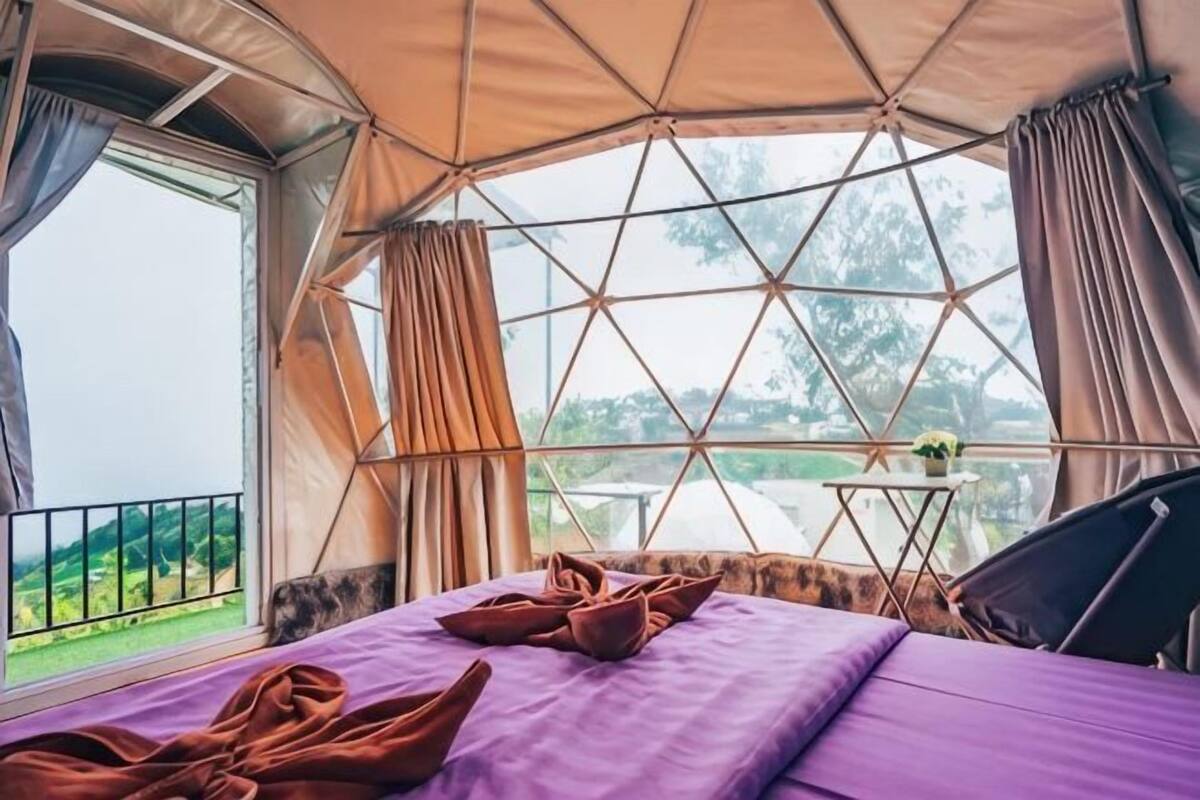 A tent-style room with a bed, curtains, and a view of greenery.