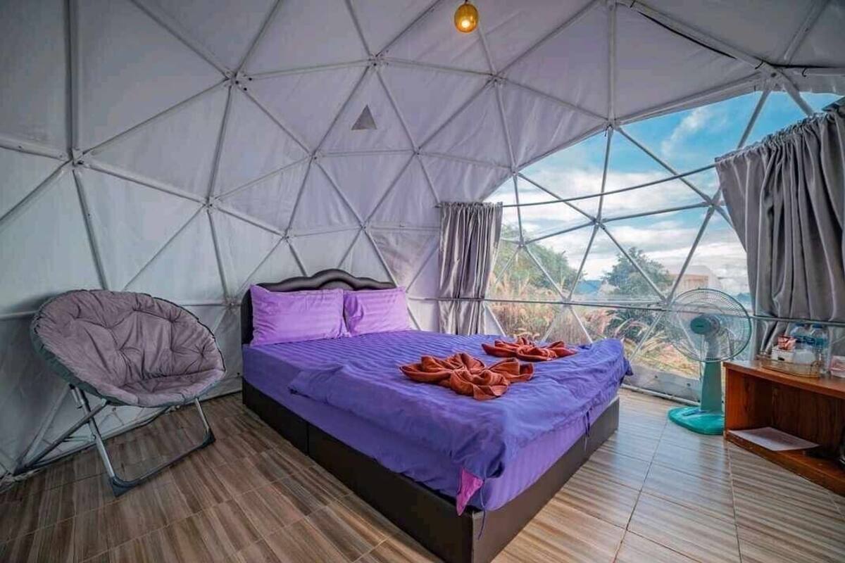 A tent-style room with a bed, a chair, and a fan.