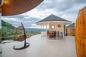 Relax in a serene outdoor space with a dining table and comfortable seating, surrounded by a hilly landscape.