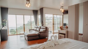 A spacious bedroom with a large bed, a sitting area with a sofa, a desk, and a view of the outdoors through large windows. - Mon Sai Lom Monjam (Mae Rim)