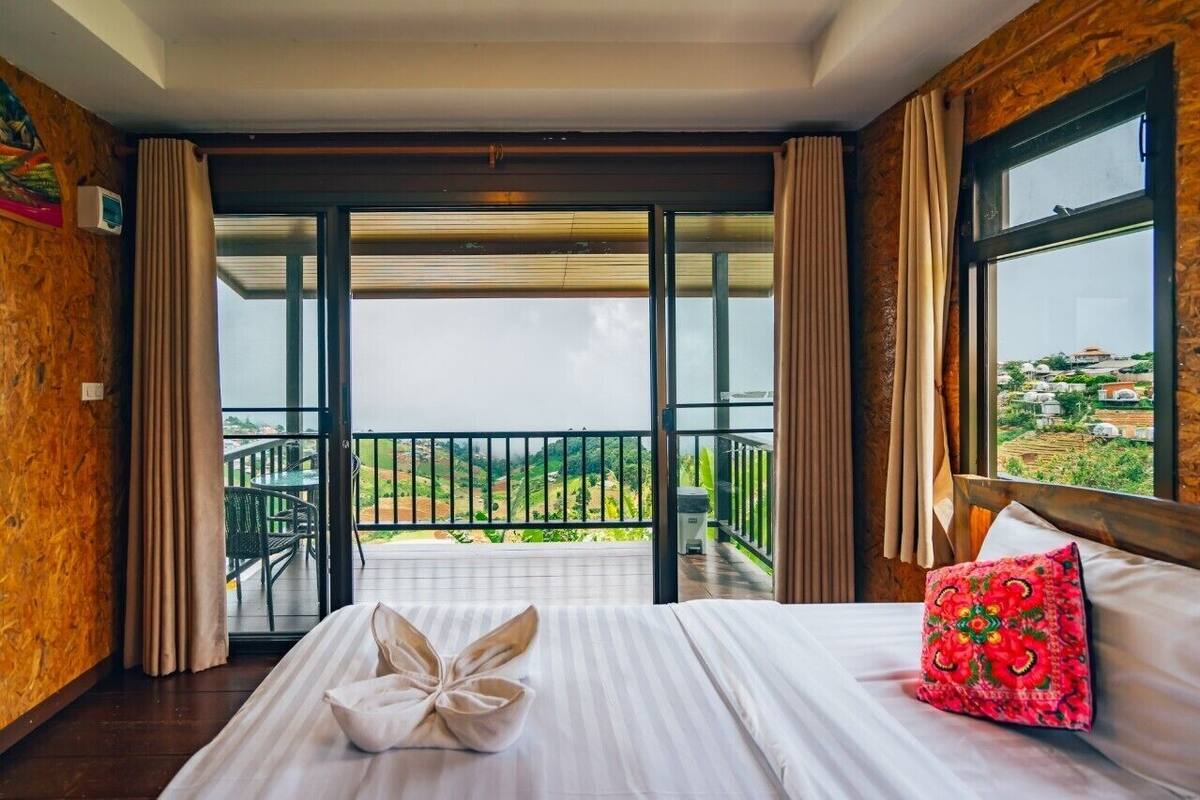 A hotel room with a bed, a balcony with a view of the countryside, and a window with curtains.