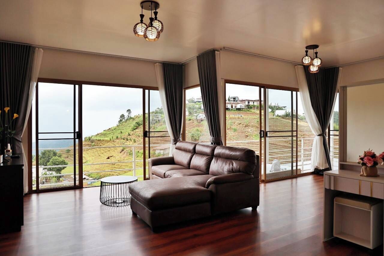 A spacious living room with a leather sofa, a round coffee table, and large windows offering a view of a hilly landscape.