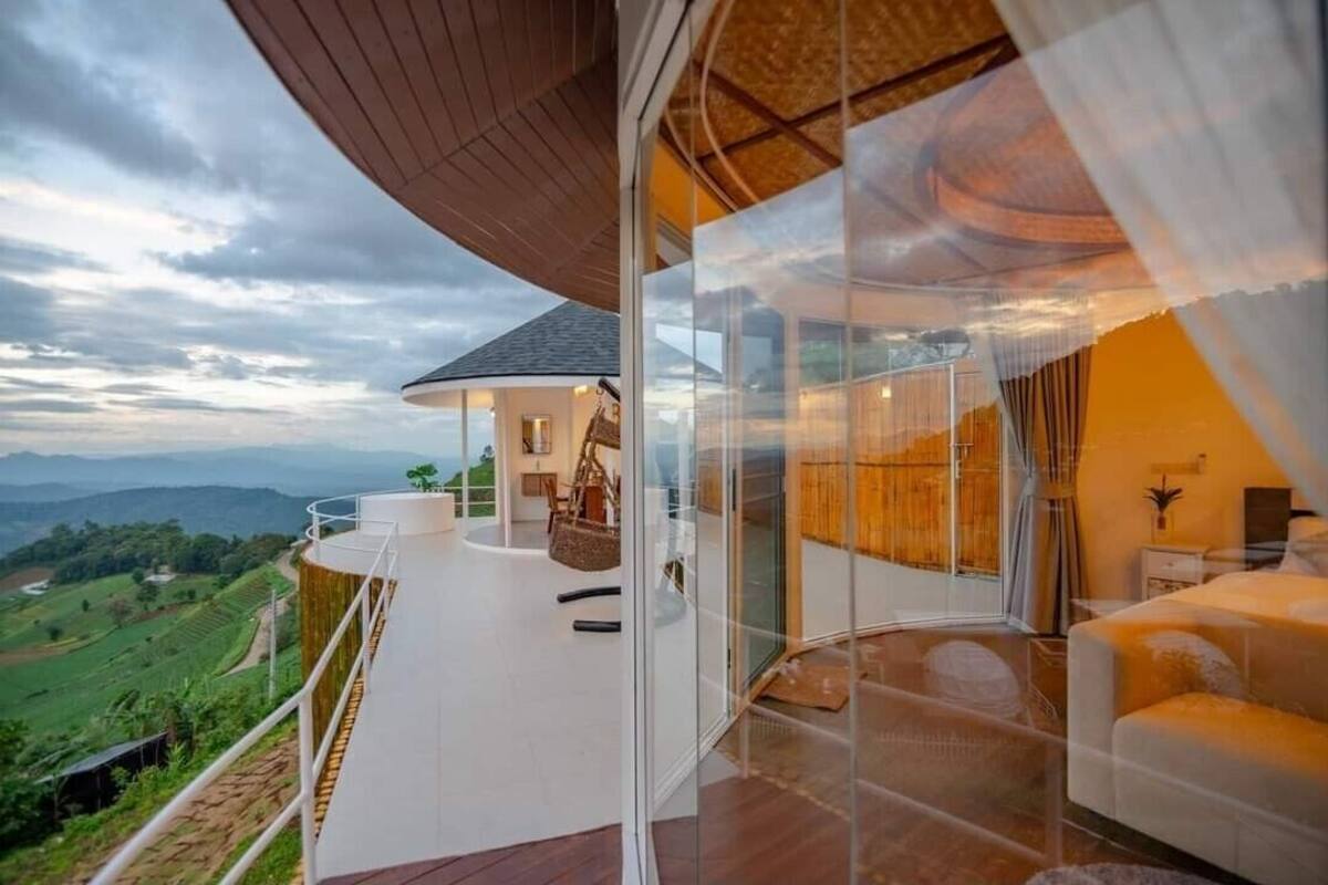 A modern, glass-enclosed balcony with a curved wooden ceiling, offering a scenic view of the countryside.