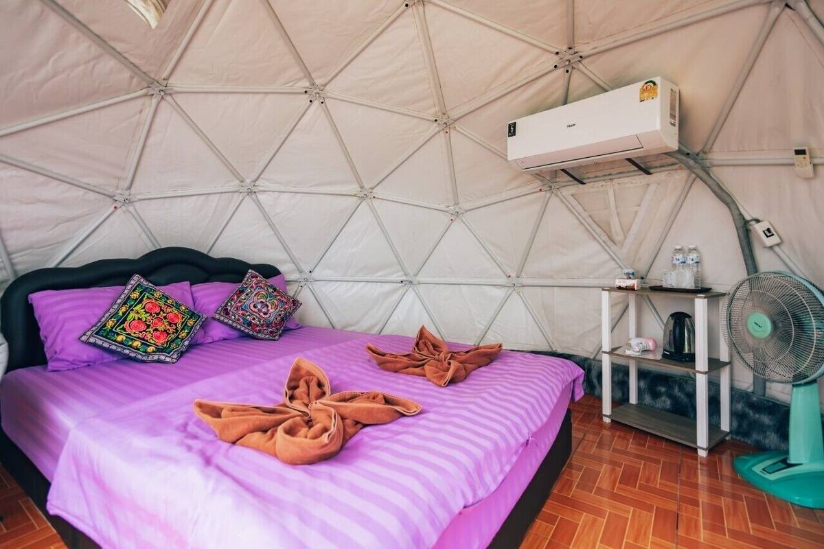 A tent-style room with a bed, air conditioning unit, and a fan.