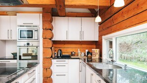 Una cocina moderna con armarios blancos, horno Bosch, microondas y lavaplatos con vista al exterior.